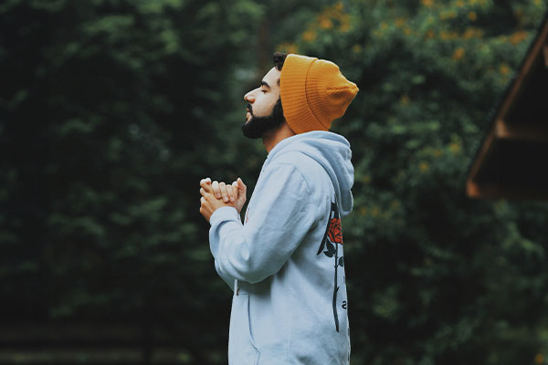 Man connected with nature with his hands in a praying position, symbolizing feeling good with christian counseling.