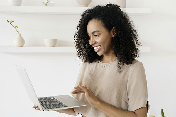 Woman at home with her laptop and smiling, getting ready to start an online counseling session in Colorado.