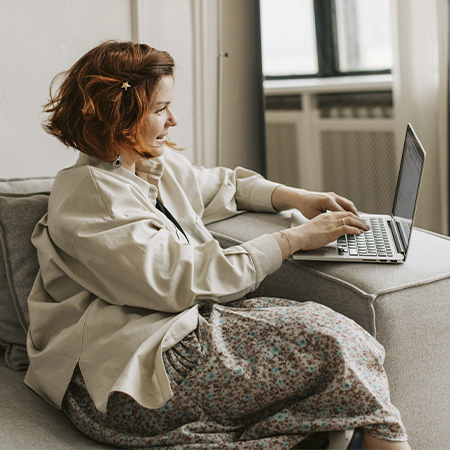 Woman sitting on the couch with a laptop, represents the positive effects of starting online therapy in Colorado.