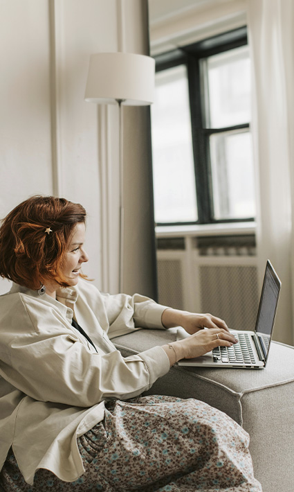 Woman sitting on the couch with a laptop, represents the positive effects of starting online therapy in Colorado.