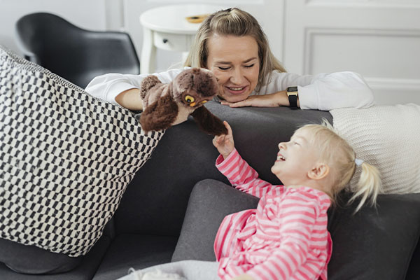 Therapist holding a hand puppet and playing with a child who's laughing, as a way to work through their issues.