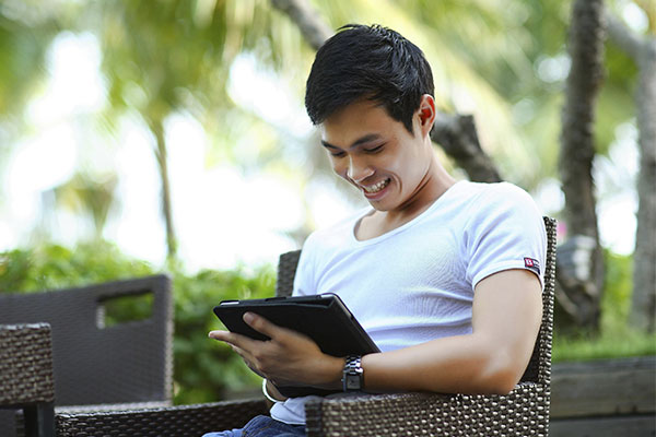 Man sitting in a terrace and smiling at his tablet. The presence of technology shows the possibilities of virtual therapy.