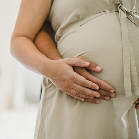 Pregnant woman with her hand and her partner's hand on her belly, preparing to start prenatal and postpartum counseling in Castle Rock, CO.