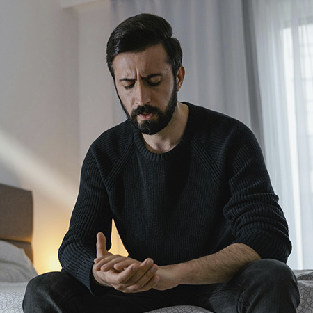 Man sitting on the bed, looking at his hands with a worried expression, before starting therapy for men in Castle Rock, Colorado.