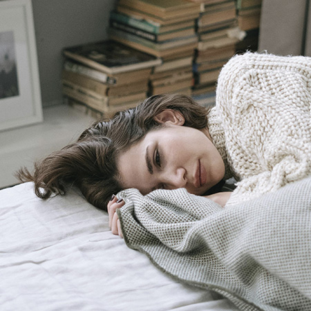 Woman with a sad expression curled up in bed, represents how you can find support for loss through grief counseling in Castle Rock, Colorado.