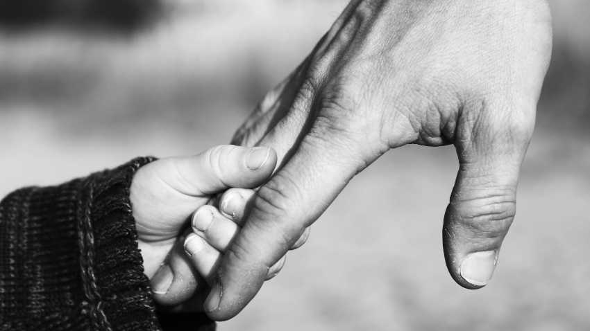 An adult hand hold a young child's hand. Representing where the young age we build our attachment styles.