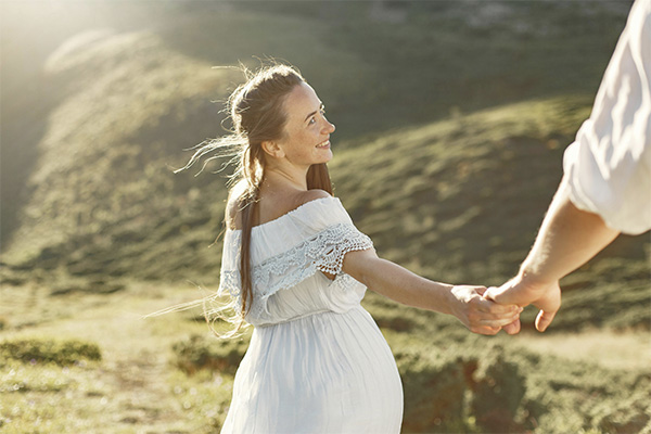 Woman in a field holding hand with her partner, represents how intensives can help you work individually or as a couple.